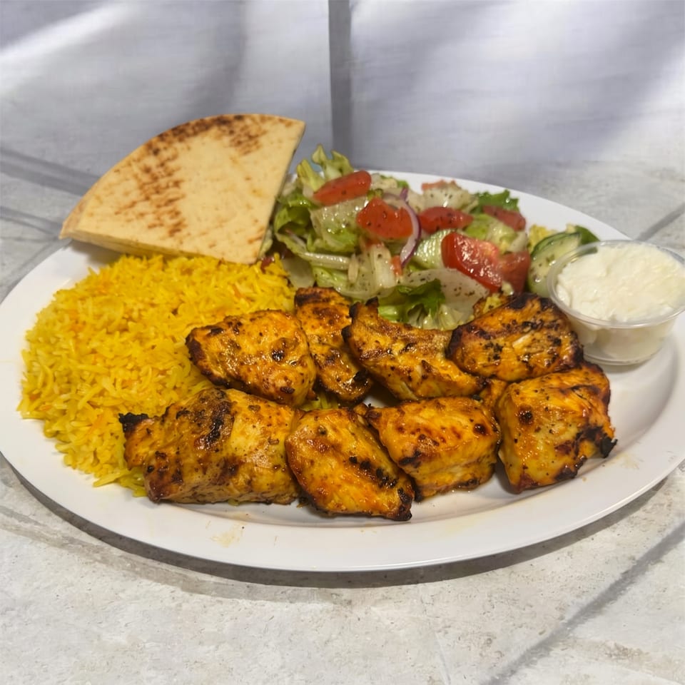 Grilled chicken pieces, yellow rice, pita bread, salad, and a side of white sauce on a plate.