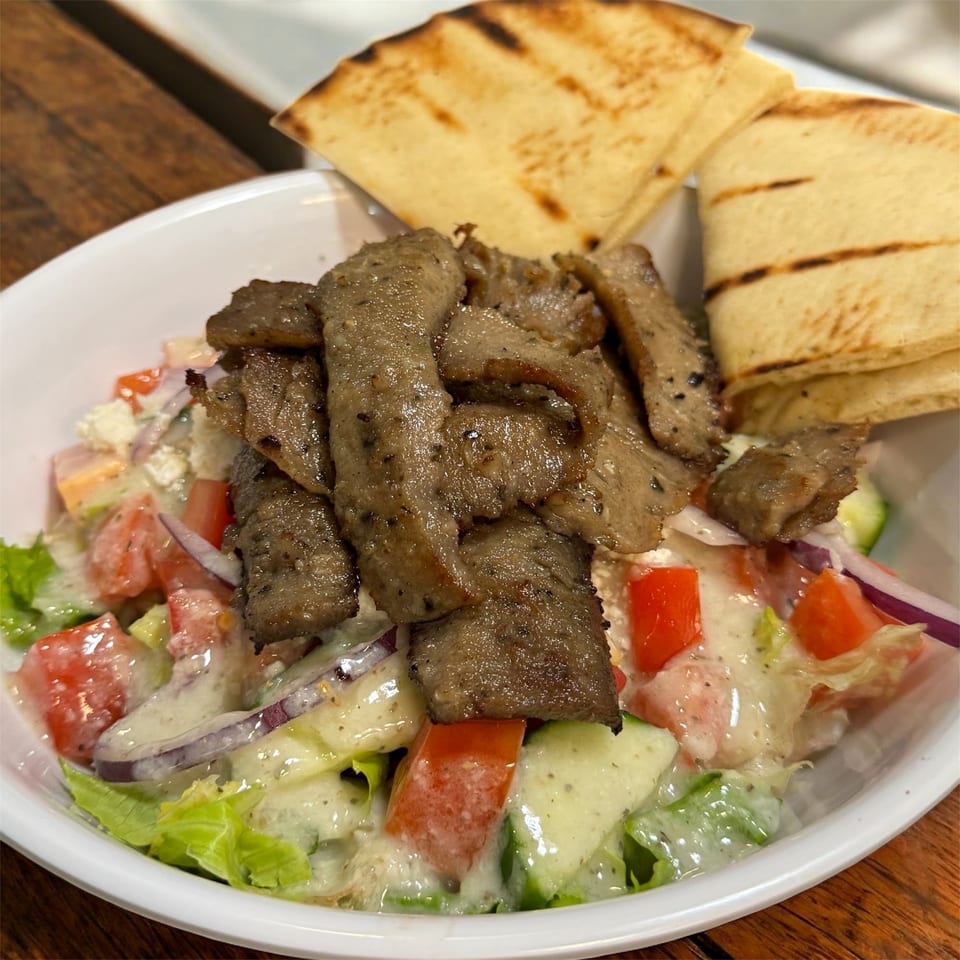 Gyro meat over a fresh salad with tomatoes, cucumbers, and onions, served with pita bread.