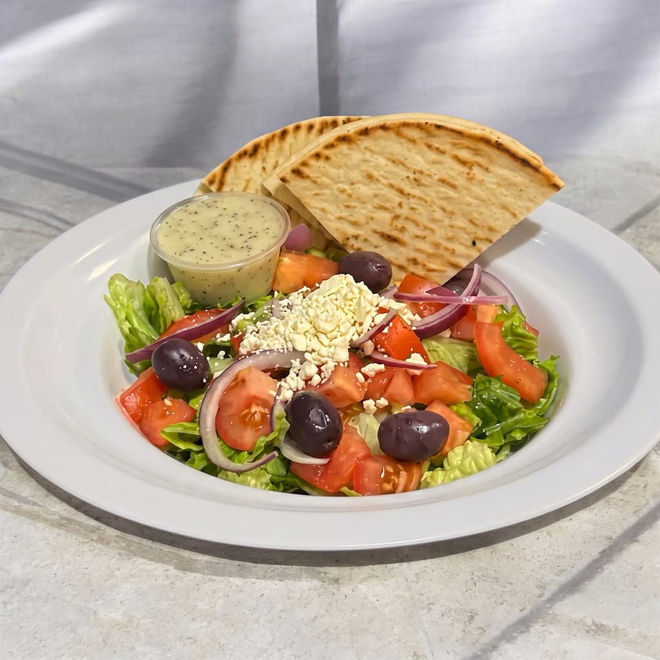 A fresh Greek salad with lettuce, tomatoes, red onions, olives, feta, and pita bread.