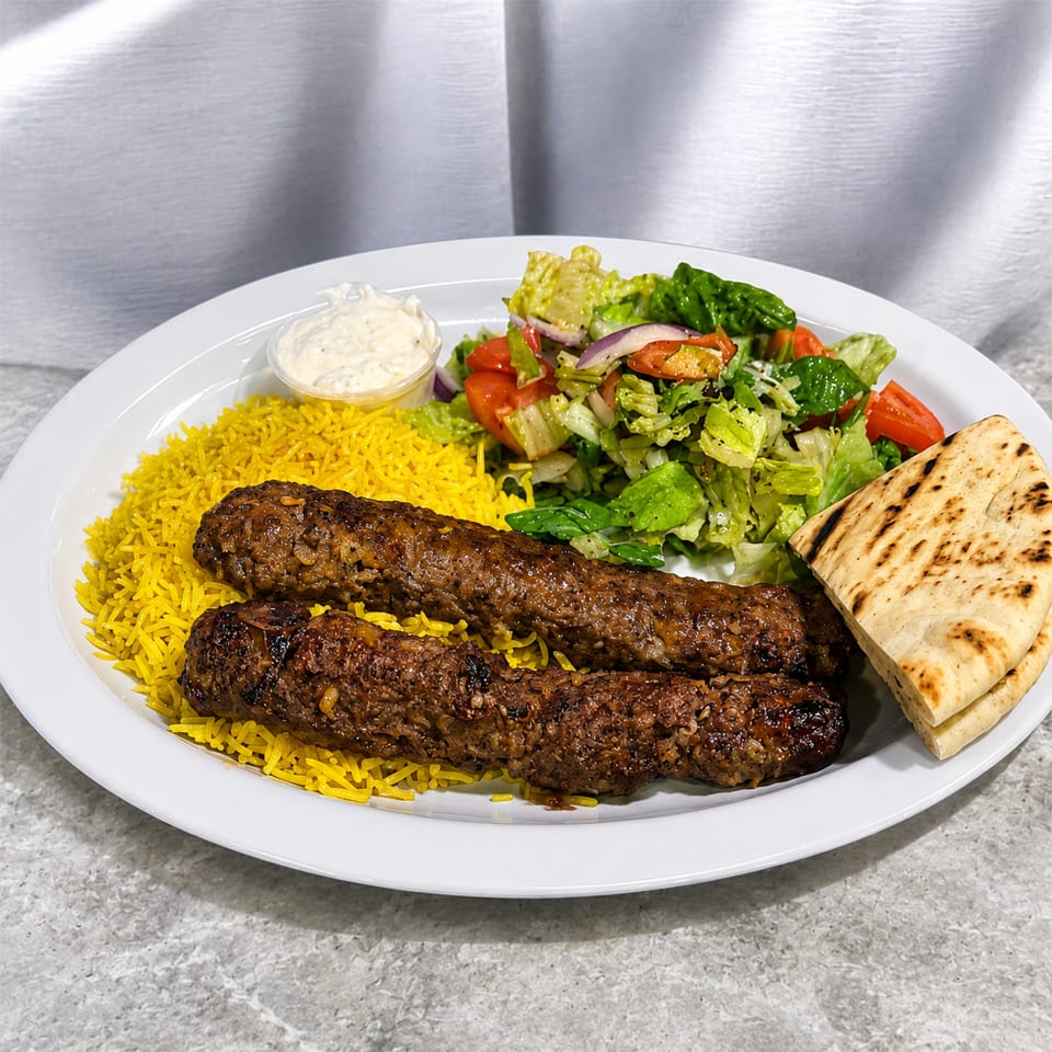 Two grilled beef kebabs, yellow rice, fresh salad, pita bread, and white sauce on a plate.
