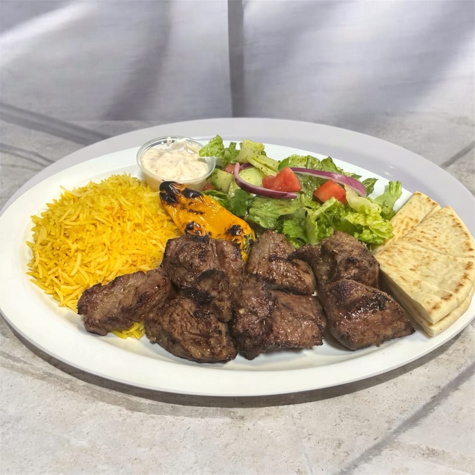 Grilled meat pieces, yellow rice, salad, pita bread, and sauce on a white plate.