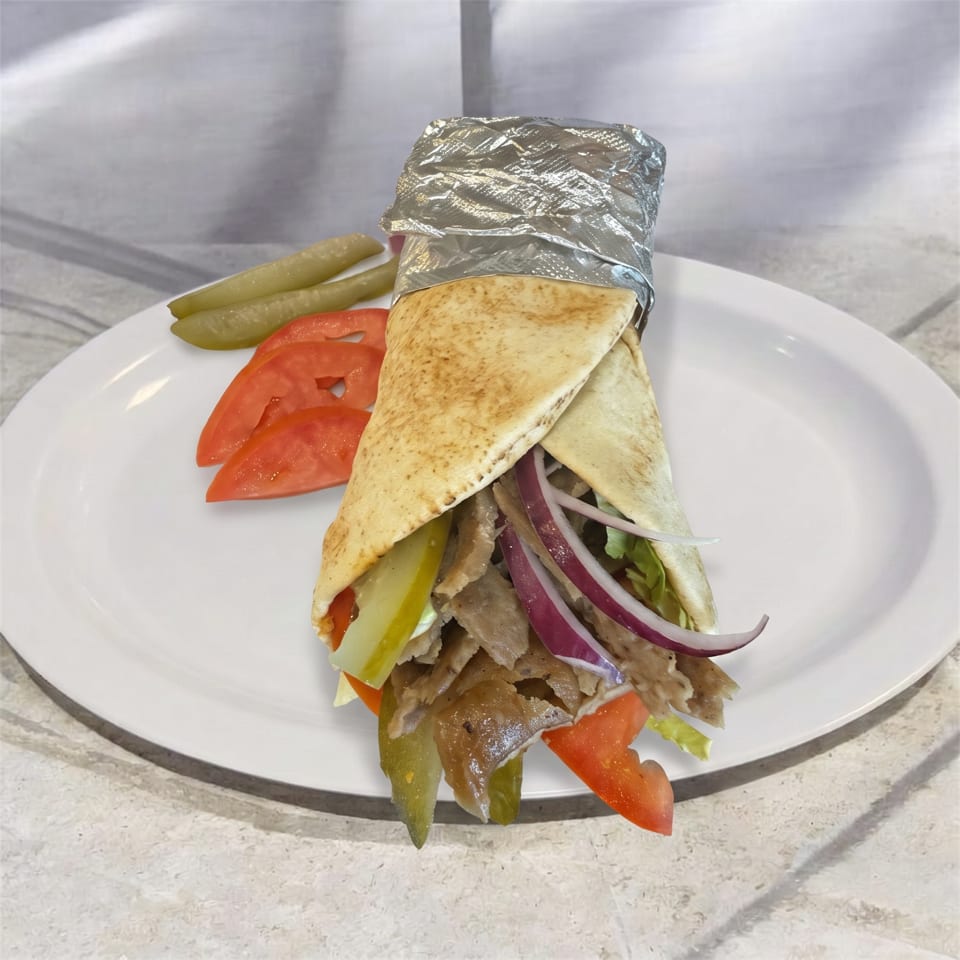 A gyro with meat, onions, and tomatoes, wrapped in pita bread and foil, served with pickles.